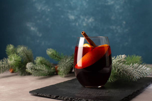 Christmas hot drink-Mulled wine with oranges,cinnamon,anise stars and cloves spice on festive Christmas background.Christmas festive card with tree branches on blue background with copy space. - Zdjęcie, obraz