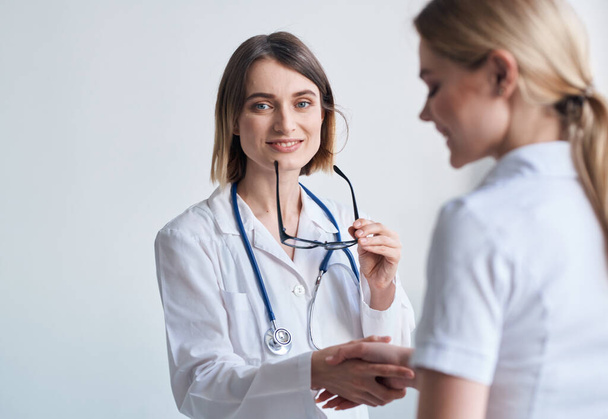 beautiful woman doctor with stethoscope shaking hands with female patient - Zdjęcie, obraz