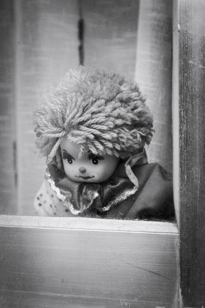 Schwarz-Weiß-Bild einer Clownspuppe, die traurig aus dem Fenster schaut - Foto, Bild