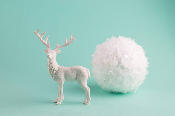 Tarjeta de felicitación minimalista Concept con ciervo blanco y gran bola de nieve decorativa sobre un fondo pastel turquesa. - Foto, imagen
