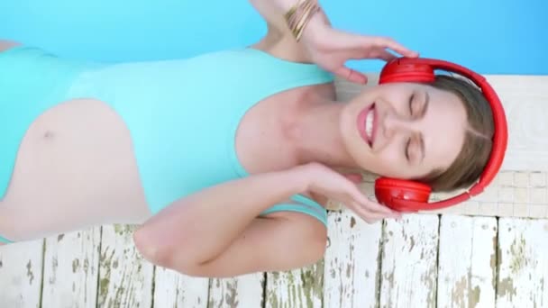 Hermosa joven escuchando música cerca de la piscina - Imágenes, Vídeo