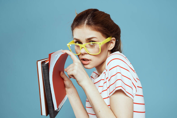 Красивая студентка с блокнотами и в желтых очках в синем учебном заведении - Фото, изображение