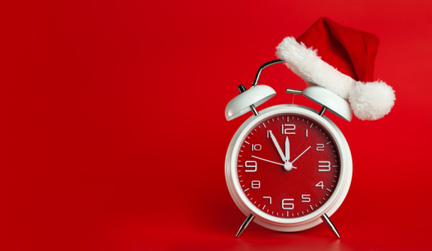 Red clock with Christmas Santa hat. Time for Christmas shopping concept. Blank red space for text. - Foto, Bild