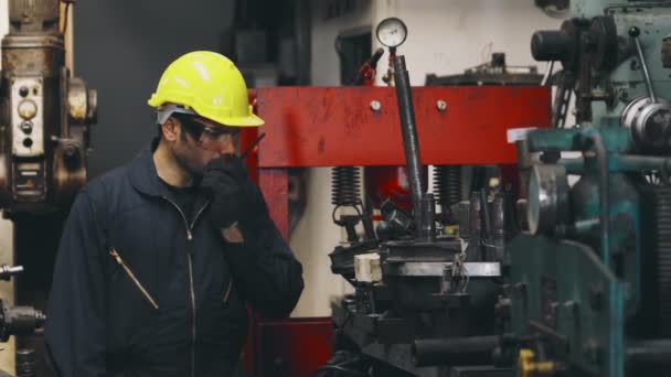 Üzemi dolgozó beszél hordozható rádión, miközben gépalkatrészeket ellenőriz - Felvétel, videó