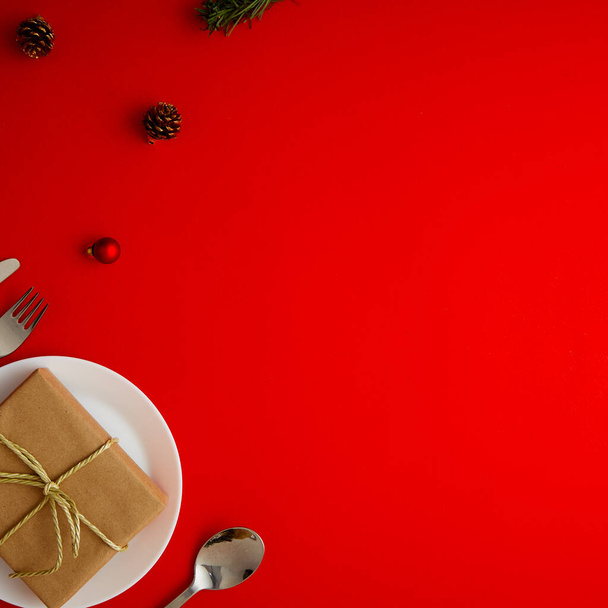 Christmas table place setting with red plate, gift box cutlery with festive decorations on a red background Top view with copy - Foto, Imagem