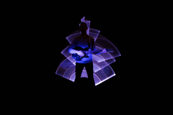 Silhouette of a man with a electric guitar. Lightpainting scene with a musical instrument and lighting effects in the background. - Photo, Image
