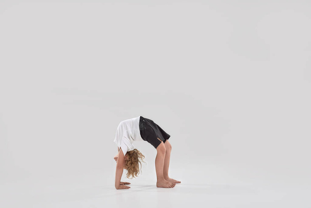 Full length shot of little playful boy child standing in bridge pose, bending over backwards isolated over grey background - Foto, immagini