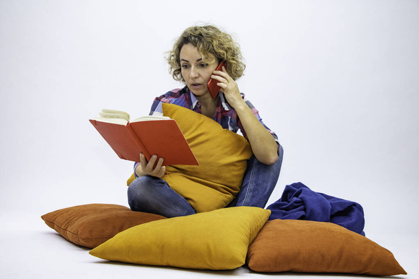 Chica sentada en el suelo de una almohada lee un libro corriente de interés de pensamiento. - Foto, imagen