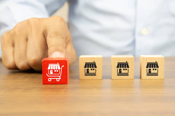 Close-up hand chooses cube wooden toy blocks stack with franchise business store icon in the shopping cart. Concepts of online e-marketplace or e-commerce franchising to growth and branch expansion strategy of financial marketing planning. - Foto, Imagem