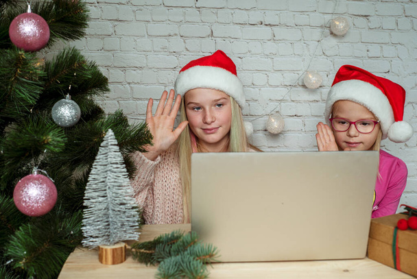 Happy girls in Santa hats waving hands while having video chat at Christmas at home - Photo, image