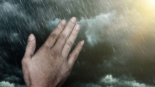 Händedruck im Gebet, Regen und Gewitterwolken, rechts ein helles Licht. Konzept des Gebets und der Hoffnung inmitten von Naturkatastrophen - schwere Regenfälle, Stürme, Taifune und anderes schlechtes Wetter. - Foto, Bild