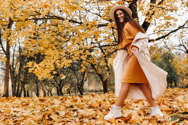 白いコートを着た陽気な女の子と秋の公園で笑顔。黄金の秋の笑顔の女性の肖像画. - 写真・画像