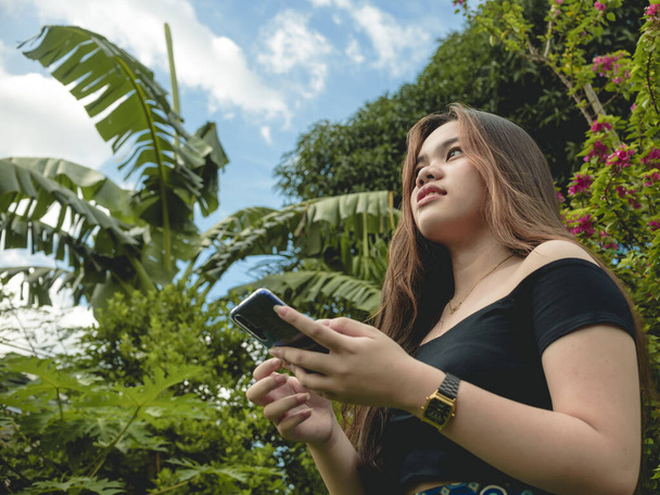 若いアジア系の若者が友達とおしゃべりしながら空を見ている。熱帯の庭の設定。インスピレーションコンセプト. - 写真・画像
