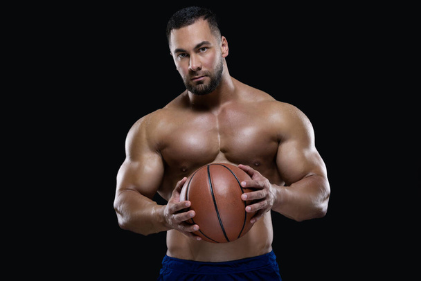 Front view portrait of an attractive sportsman holding a basketball with both hands isolated on black background - Foto, Imagen