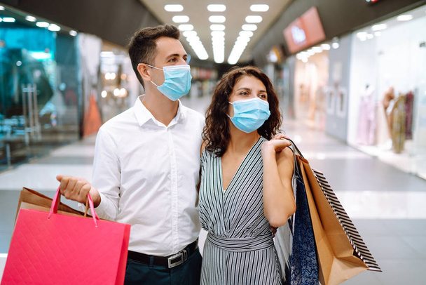 Portrait of a couple with shopping bags in protective sterile medical mask in mall. Shopping in the coronavirus pandemic. People, sale, love, black friday and happiness concept. - Foto, imagen