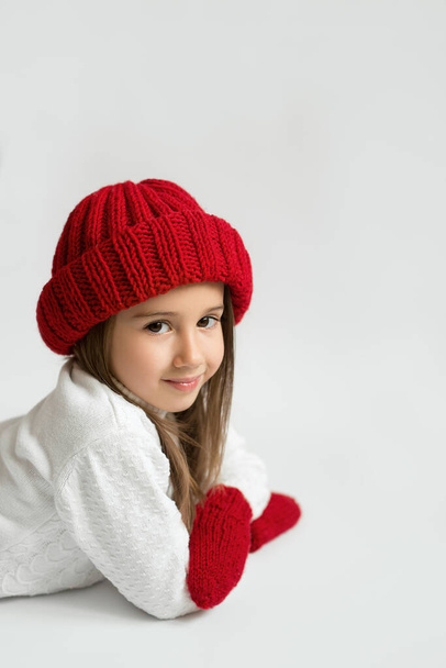 Χαριτωμένο κοριτσάκι με κόκκινο καπέλο και γάντια σε λευκό φόντο - Φωτογραφία, εικόνα
