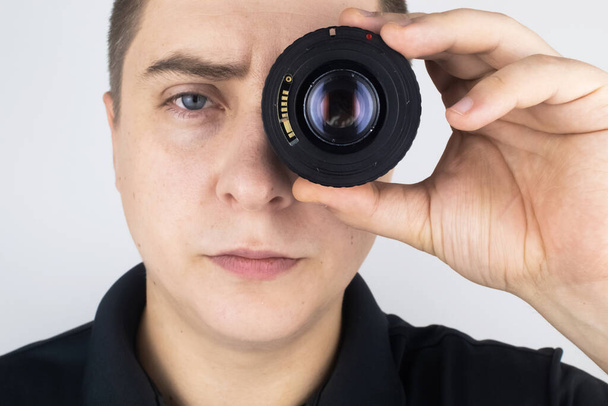 Um homem experimenta uma lente de câmera em vez de um olho. O conceito do trabalho do fotógrafo e a abordagem criativa da fotografia - Foto, Imagem