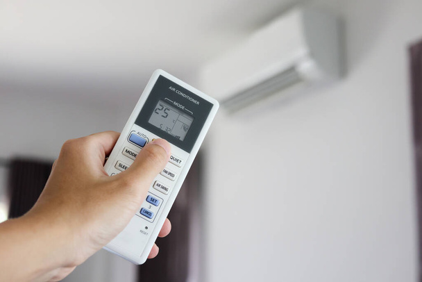 Hand met afstandsbediening gericht op airconditioner in de kamer - Foto, afbeelding