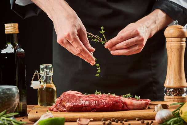 Chef throwing thyme leaves onto meat. Professional cook seasoning beef steak - Foto, Bild