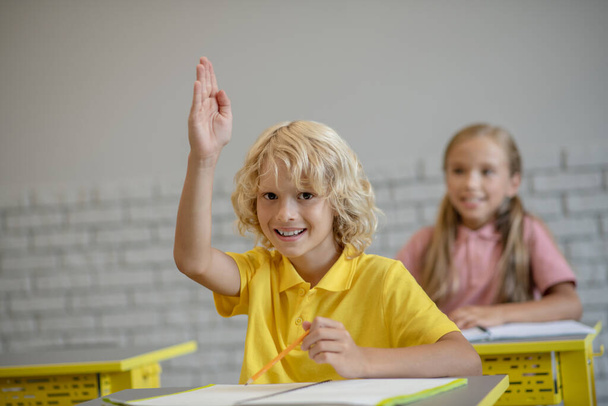 Blonde boy raising his hand ready to answer - Foto, Bild