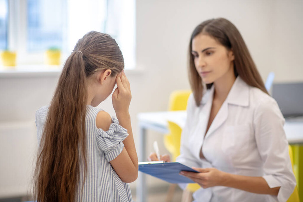Girl having a headache and talking to the doctor - Photo, Image