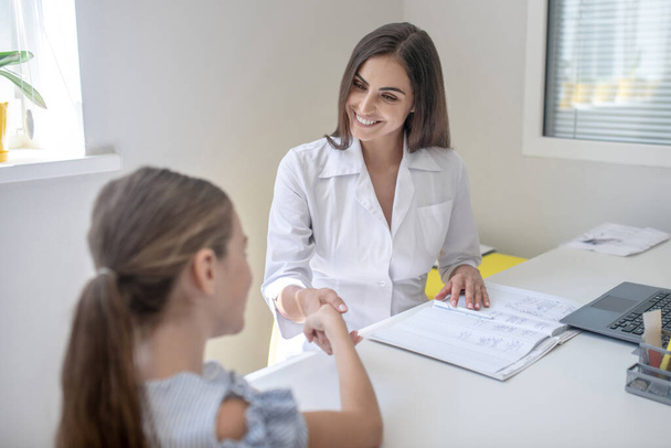 Girl sitting at the table and talking to a doctor - Foto, imagen