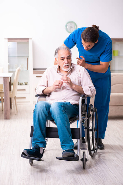 Старий в інвалідному кріслі і молодий поганий доглядач в приміщенні
 - Фото, зображення