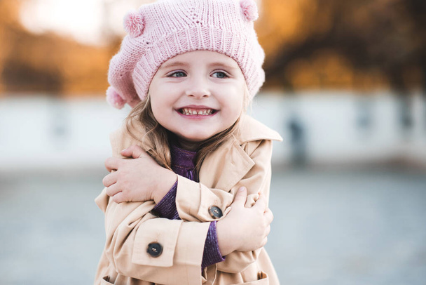Onnellinen lapsi tyttö 3-4 vuotias yllään syystakki ja knited hattu luonnon taustalle lähikuva. Syyskausi. Lapsuus.  - Valokuva, kuva