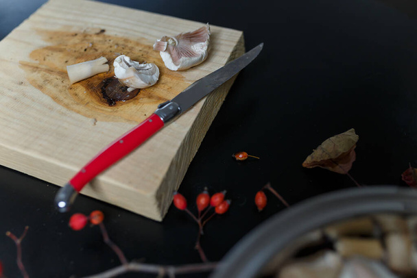 黒い木製のテーブルの上に金属製のボウルに生のシャンパンをカット.まな板にキノコのスライスが付いた赤いナイフ。健康的な有機ベジタリアン食品。食事、栄養の概念。スペースのコピー - 写真・画像