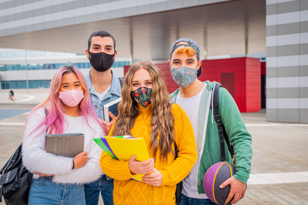 Образование, здравоохранение и пандемия - группа студентов-универсалистов в защитных медицинских масках для защиты от вирусных заболеваний с рюкзаками, ходящими и разговаривающими на открытом воздухе - Фото, изображение