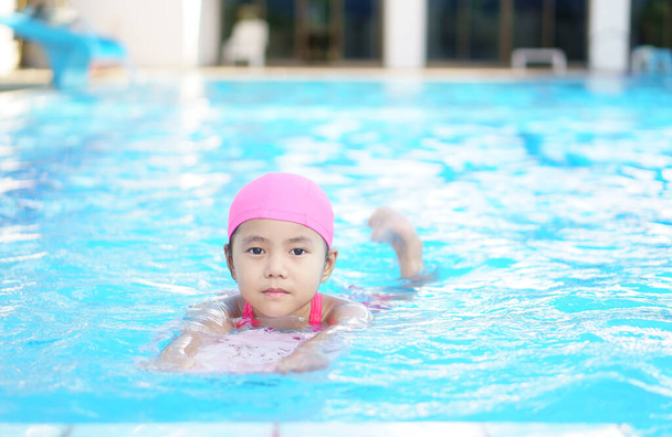Asian child cute or kid girl smile wearing swimming suit on school swimming pool and happy fun in water park for learn and training swim on kick board or refreshing relax to exercise on summer holiday - Photo, Image