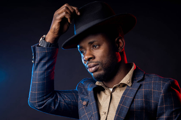 Handsome serious business African American man in hat on black background with blue and red lights in Studio, copy space - 写真・画像