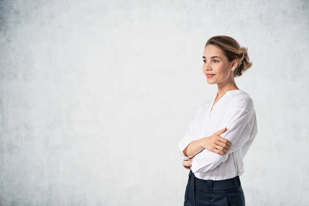 Portrait of smiling young European businesswoman looking forward standing near concrete wall. Mock up - Photo, image