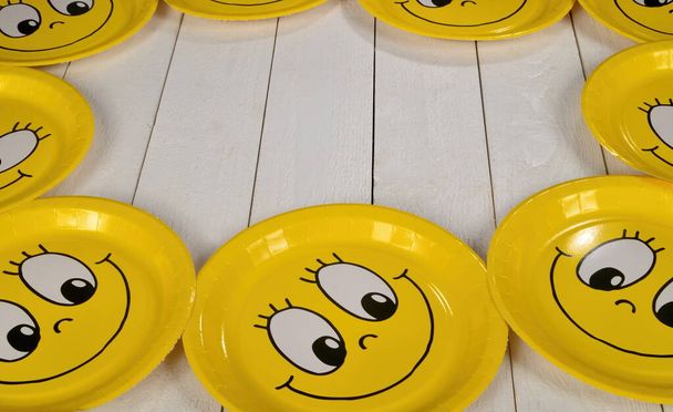 Happy smiley cartoon face on yellow paper plate. White wooden background. Happy yellow emoticon smiling - Foto, afbeelding