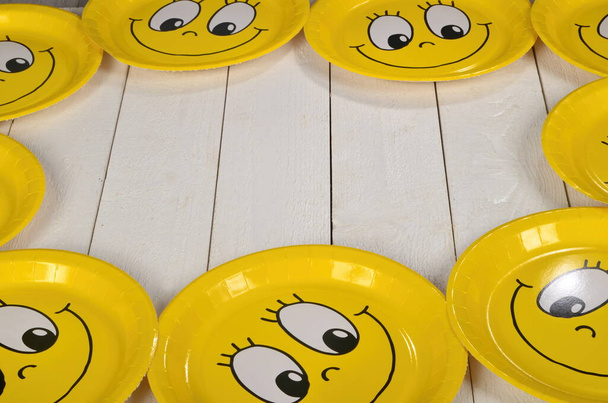 Cara de dibujos animados sonriente feliz en placa de papel amarillo. Fondo de madera blanca. Feliz emoticono amarillo sonriendo - Foto, imagen