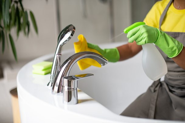 Professional cleaning of the bathroom and toilet. Cleanliness and hygiene at home. Cleaning service and housekeeping. Hand in green and yellow latex gloves. Rubbing the bathroom and taps - Photo, image