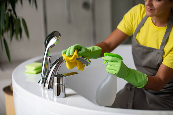 Limpieza profesional del baño y aseo. Limpieza e higiene en el hogar. Servicio de limpieza y limpieza. Mano en guantes de látex verde y amarillo. Frotar el baño y grifos - Foto, imagen