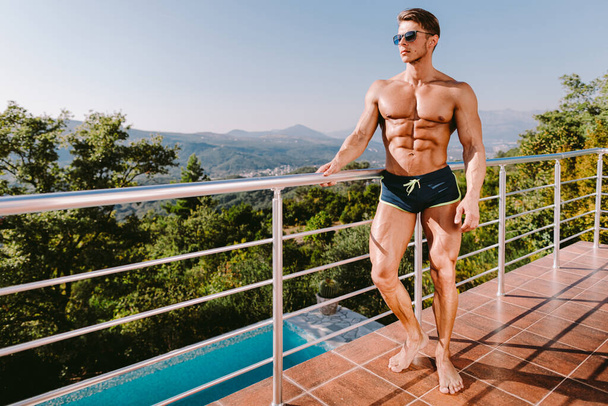 Retrato de moda de un hombre musculoso en bañador en la piscina - Foto, Imagen
