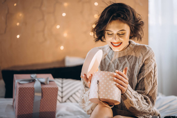 Happy and pretty brunette on the bed with gift boxes around her. New Year, Christmas, birthday, Valentine Day concept - Photo, Image