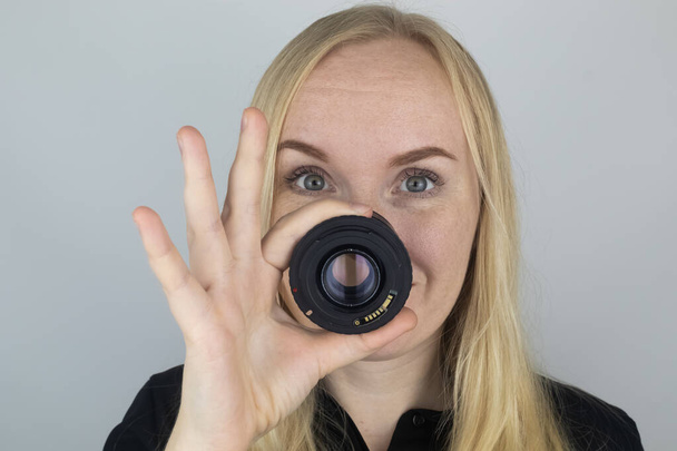 Una mujer se prueba una lente de cámara en lugar de una nariz. El concepto del trabajo del fotógrafo y el enfoque creativo de la fotografía - Foto, Imagen