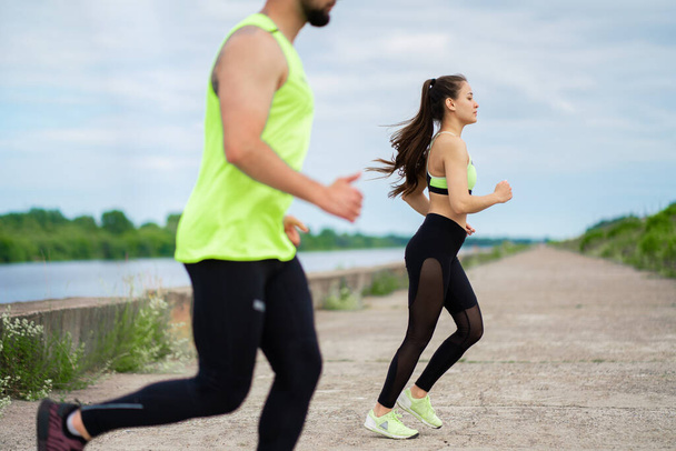 Running young couple in stylish sportswear on workout outdoor in cloudy weather, cropped photography - Foto, Bild
