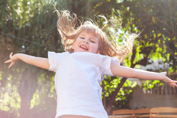 幸せな女の子が興奮し、髪を飛んで、腕を広げてジャンプします。陽気で熱狂的な笑いの子供は日光、幸福、楽しさと健康的なアクティブな休日のライフスタイルの概念に飛び込む - 写真・画像