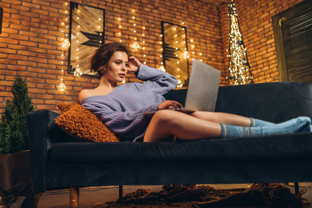 Pretty young brunette at home on the couch using laptop, online education, studying, shopping, working concept - Zdjęcie, obraz