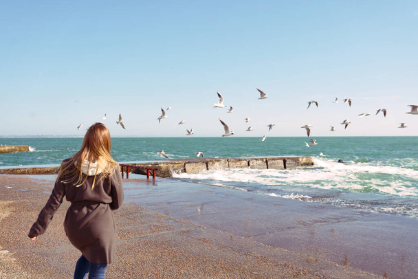 Frau mit blonden langen Haaren läuft im Winter mit Möwen am Strand - Foto, Bild