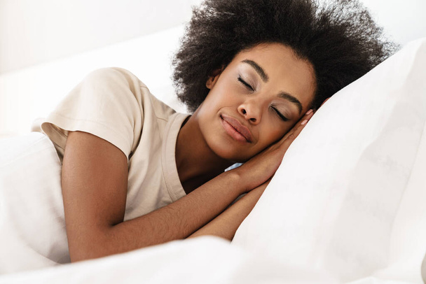 Smiling beautiful young african woman sleeping in bed, eyes closed - Valokuva, kuva
