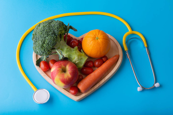 World diabetes day concept with clean fruits in nutritionist's heart dish. Yellow stethoscope on blue color background - Φωτογραφία, εικόνα