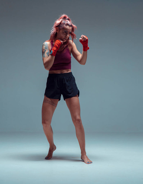 Female fighter trains in boxing bandages in studio on gray background. - Fotó, kép
