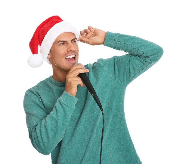 Emotional man in Santa Claus hat singing with microphone on white background. Christmas music - Foto, Imagen