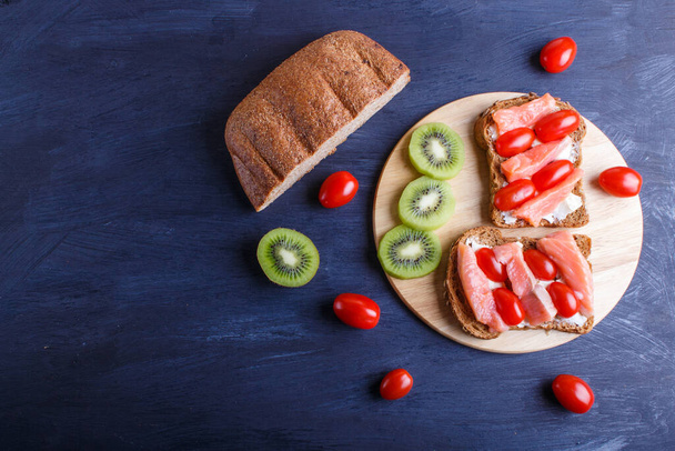 Uzené lososí sendviče s máslem na tmavém dřevěném pozadí. cherry rajčata. horní pohled, kopírovací prostor. - Fotografie, Obrázek