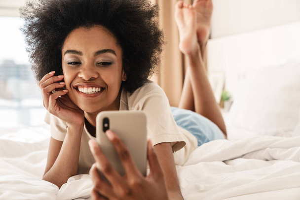 Happy young african woman taking a selfie while laying in bed - Foto, imagen